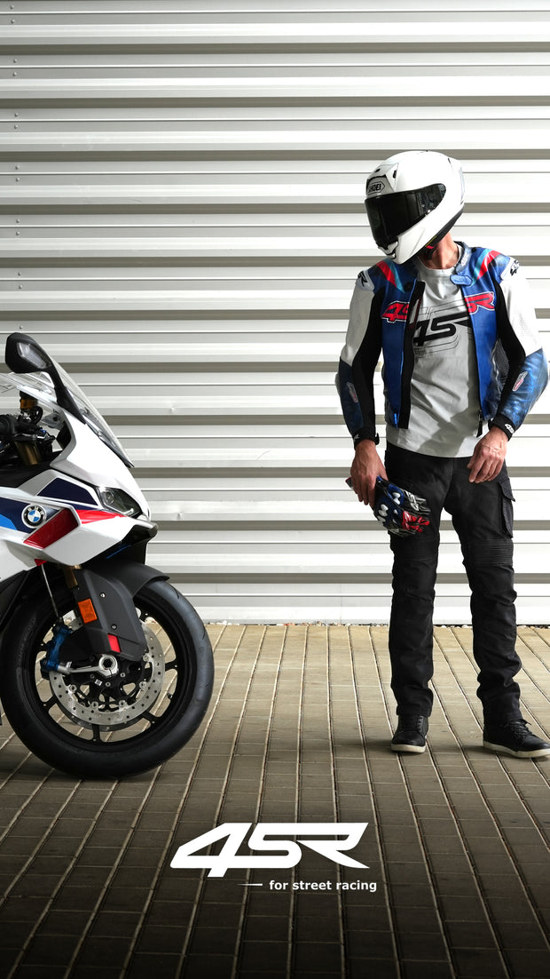 Rider in 4SR RR Blue AR leather jacket and Tourismo Black motorcycle jeans standing beside a BMW sportbike, showcasing full riding gear.