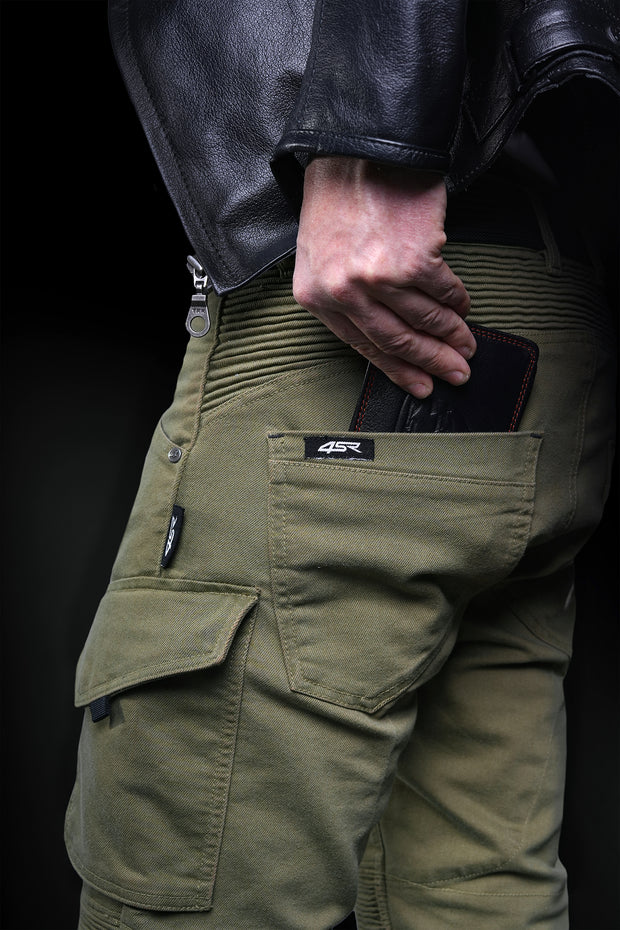 Close-up of 4SR Tourismo Green motorcycle jeans – rider placing wallet into secure rear pocket with flex panels visible