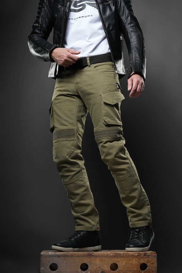 ider wearing 4SR Tourismo Green motorcycle jeans made from durable Cordura® denim, featuring ergonomic knee shaping, cargo pockets, and flex panels for comfort. Styled with a leather jacket and riding shoes.