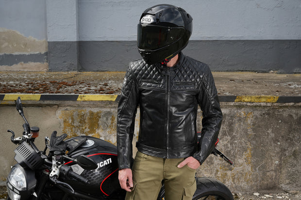 Rider wearing 4SR Scrambler Petroleum II black leather jacket with Level 2 protectors, standing by Ducati motorcycle