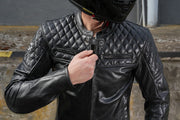 Lifestyle photo – rider adjusting zipper -Motorcyclist wearing 4SR Scrambler Petroleum II leather jacket, adjusting the zipper while wearing a helmet.